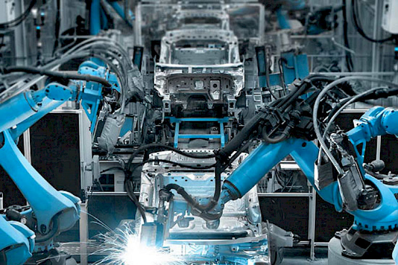 Blue industrial robot arms welding in a vehicle automation system.