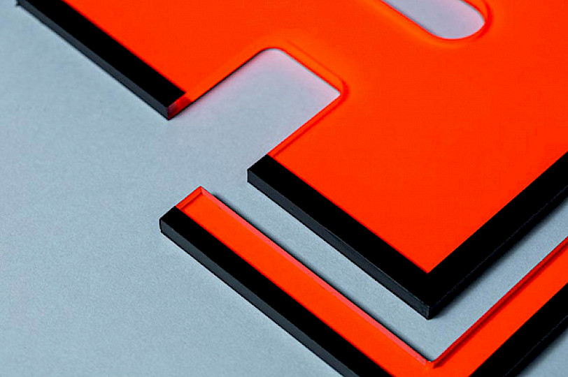 Orange acrylic panel with black edge on a gray surface.